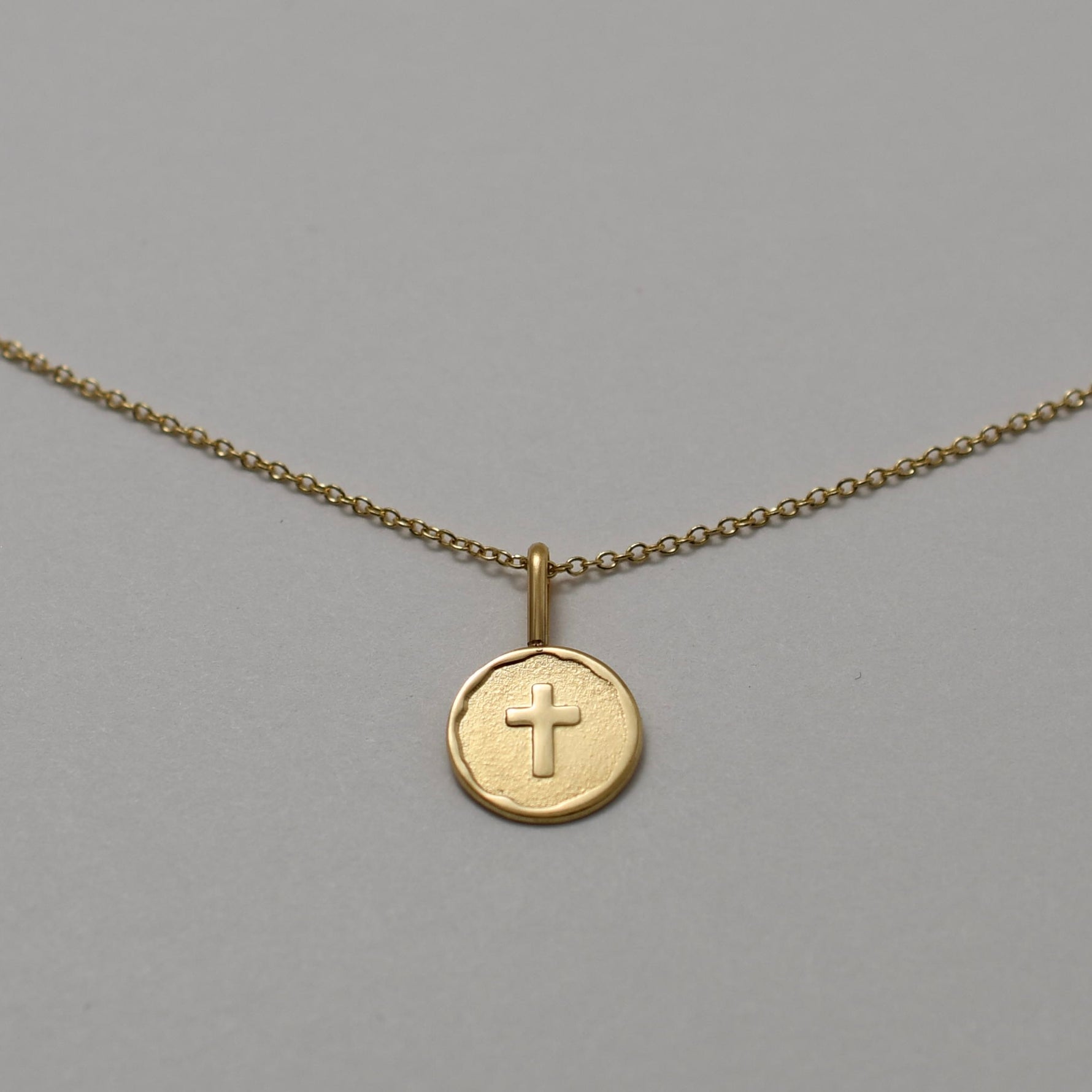 Gold necklace with a round pendant featuring a cross on a gray background