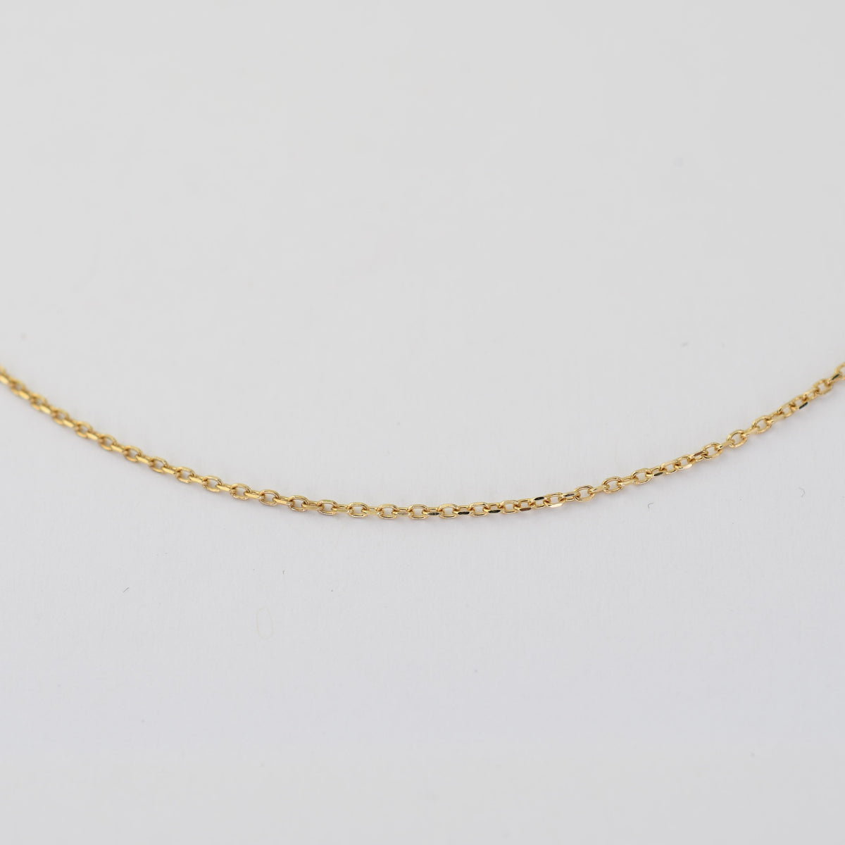A delicate gold chain necklace displayed in a gentle curve against a plain white background.
