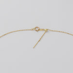 Close-up of a gold chain necklace showing the clasp, lobster clasp, small bead, and a dangling bar extender on a light gray background.