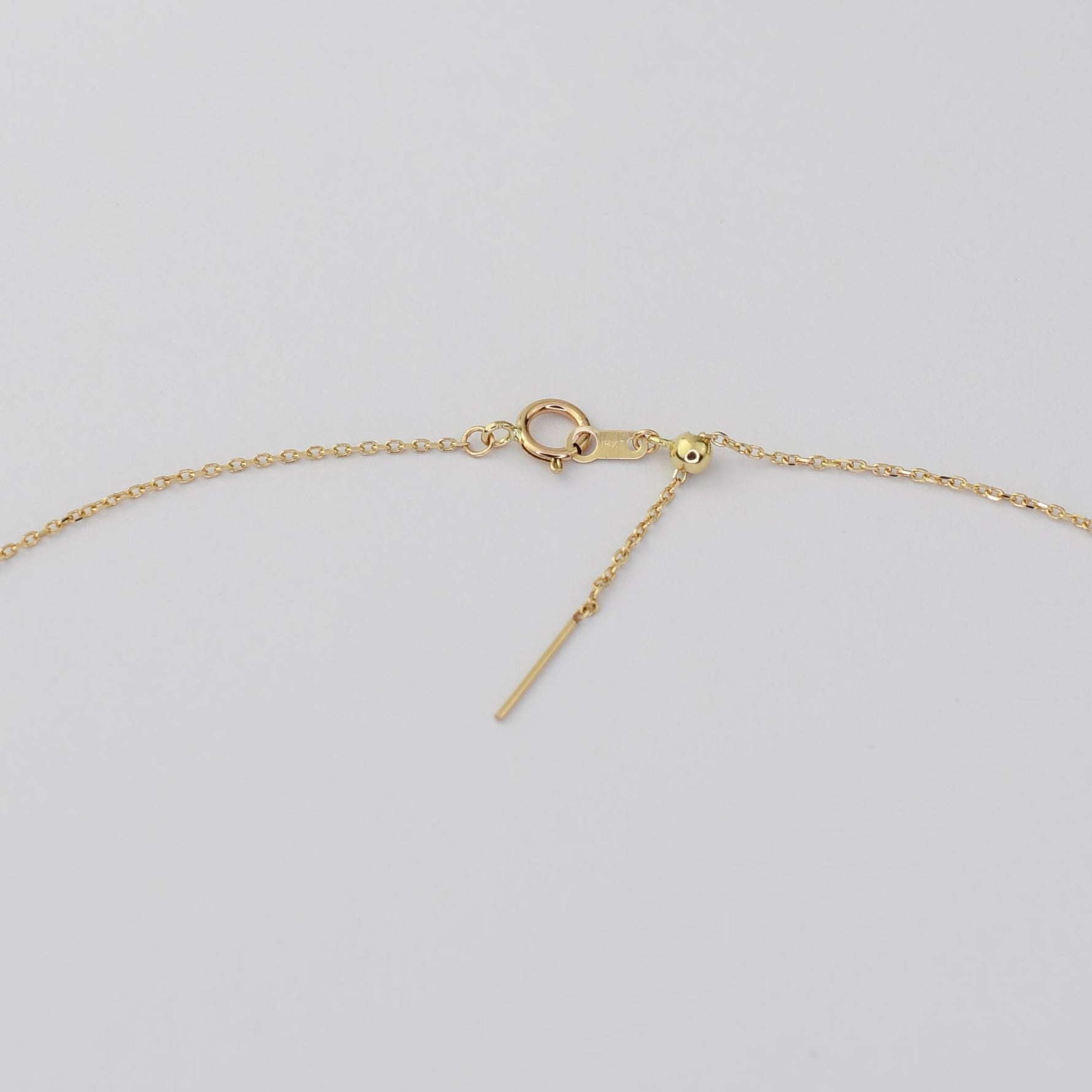 Close-up of a gold chain necklace showing the clasp, lobster clasp, small bead, and a dangling bar extender on a light gray background.