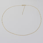 A delicate gold chain necklace with a small central knot detail, displayed on a plain light gray background.