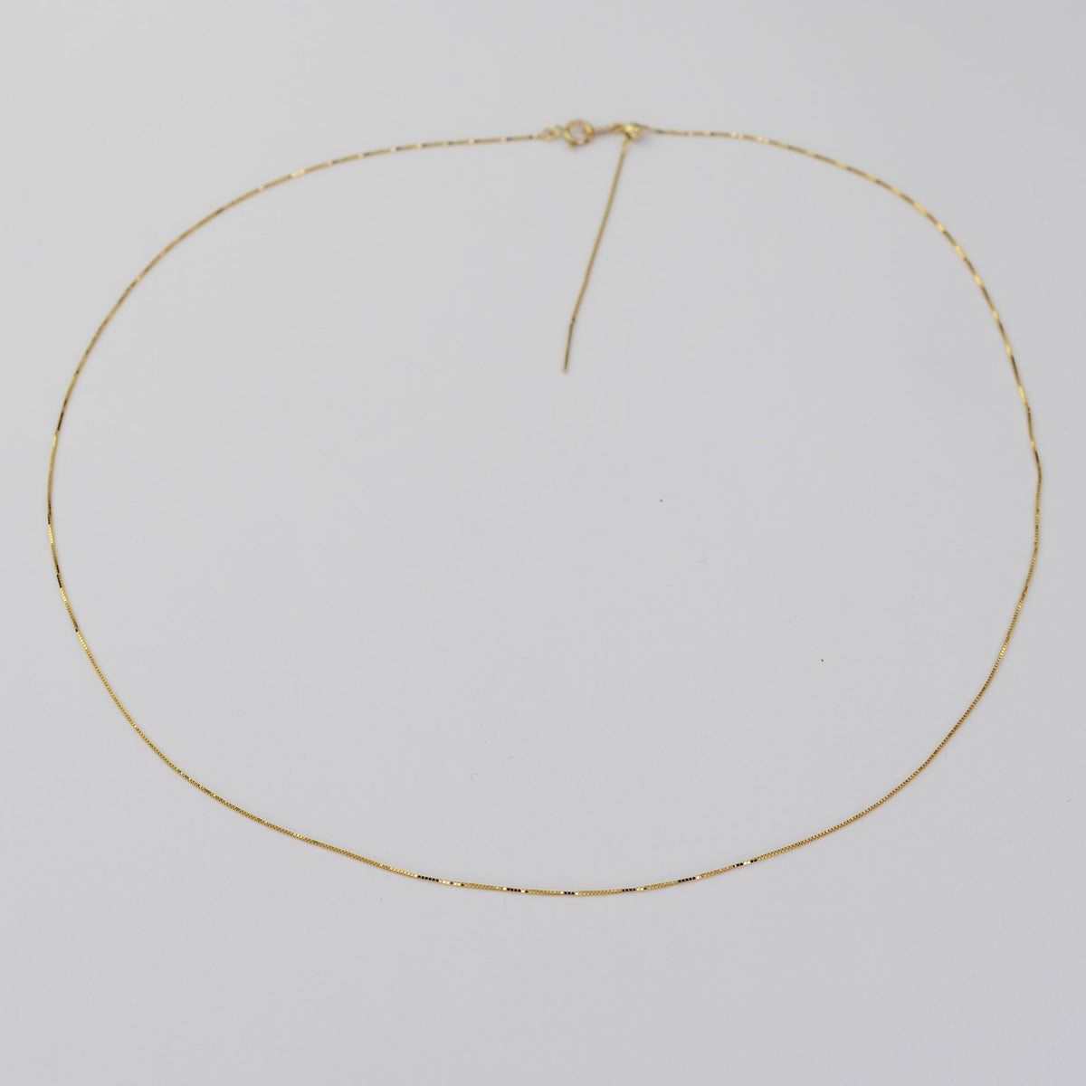 A delicate gold chain necklace with a small central knot detail, displayed on a plain light gray background.