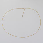 A delicate gold chain necklace with a small textured clasp, laid flat in a circle on a light gray background.