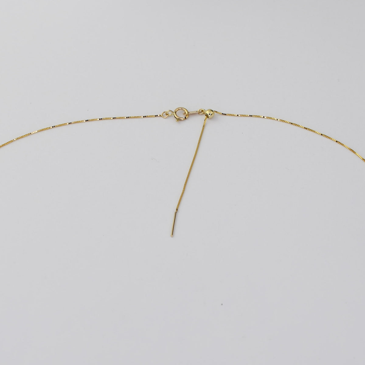 A close-up of a gold chain necklace showing the clasp, extender, and loop end against a plain light gray background.