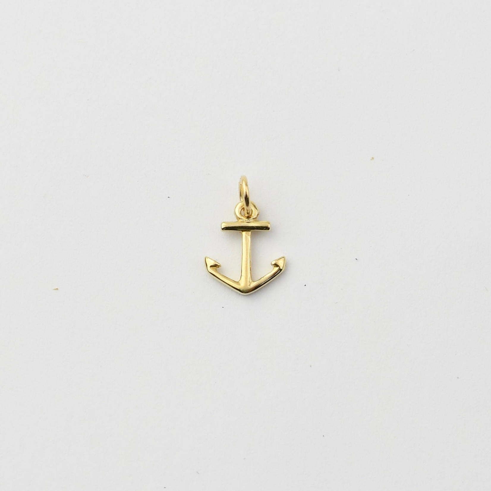 A small gold anchor charm with a top loop, shown on a plain light gray background.