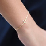Gold anklet with an anchor charm on a person's ankle against a dark background