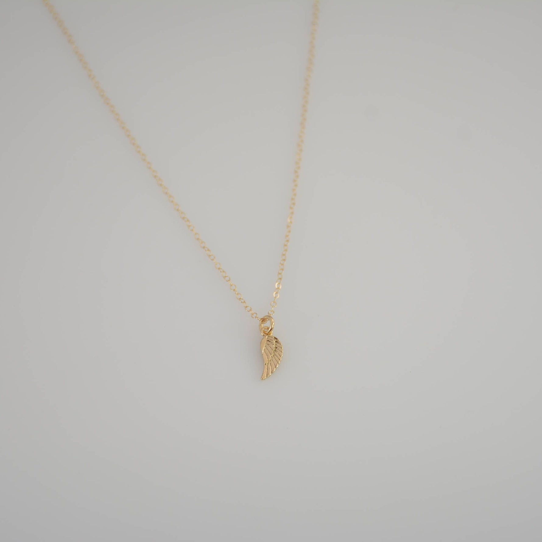 Gold necklace with a small pendant on a light gray background