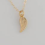 Gold angel wing necklace on a light gray background