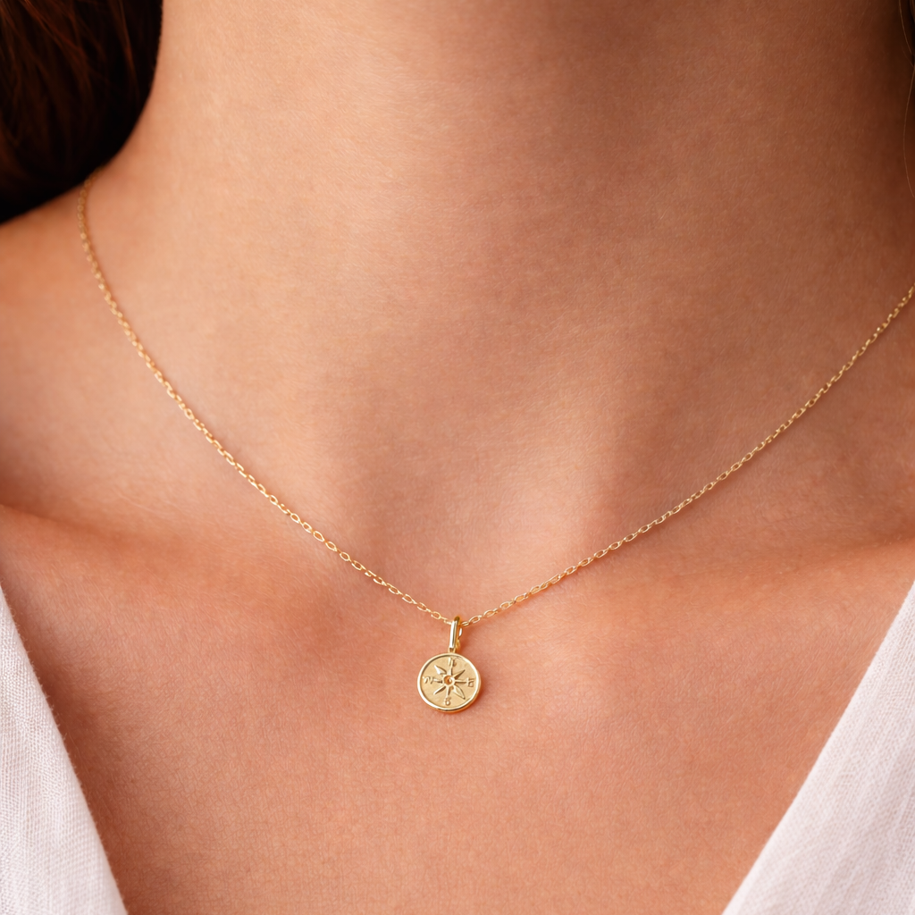 Gold necklace with a round pendant on a person wearing a white top.