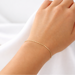 Hand wearing a gold bracelet on a white fabric background
