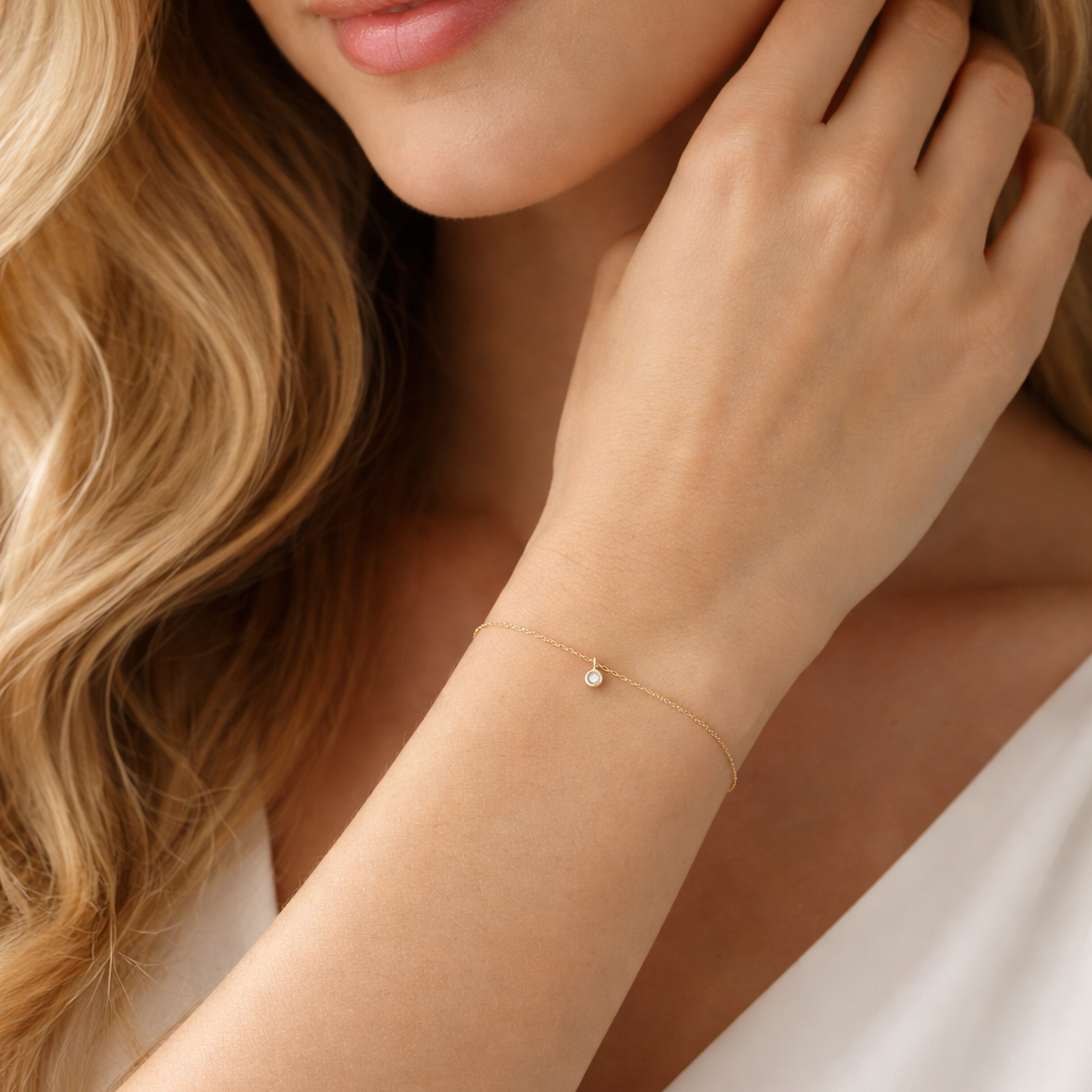 Close-up of a woman wearing a delicate gold bracelet on a neutral background