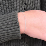 Silver bracelet on a person's wrist with a gray textured sweater sleeve.