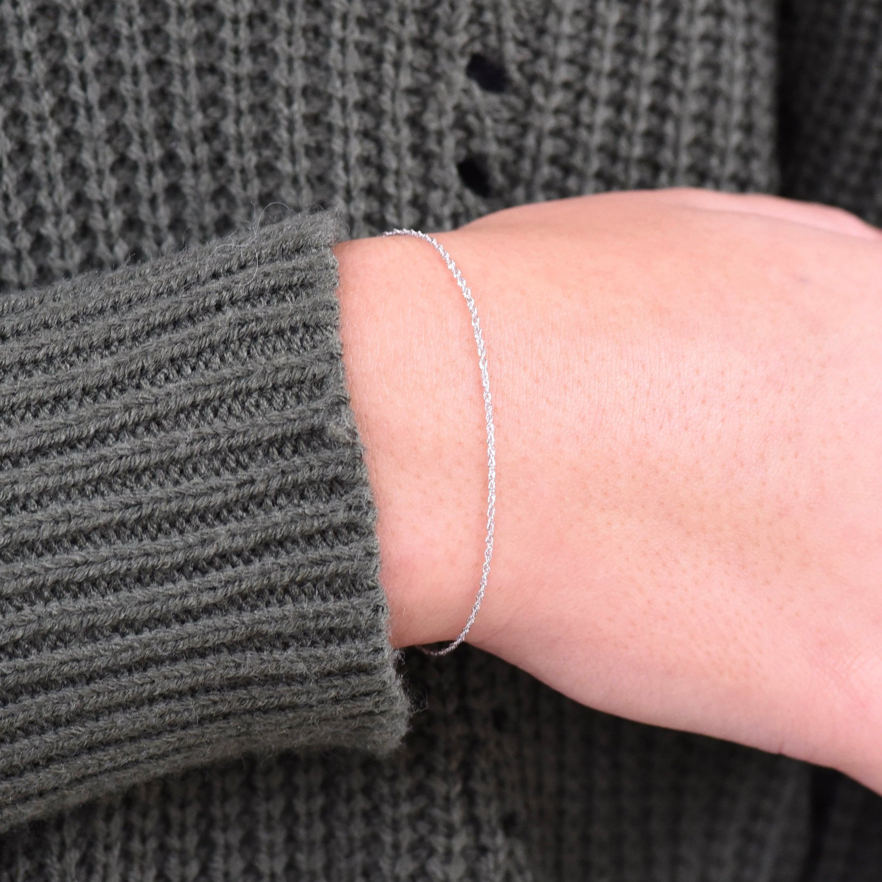 Silver bracelet on a person's wrist with a gray textured sweater sleeve.