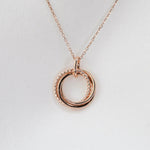 Rose gold necklace with a double circular pendant on a light gray background