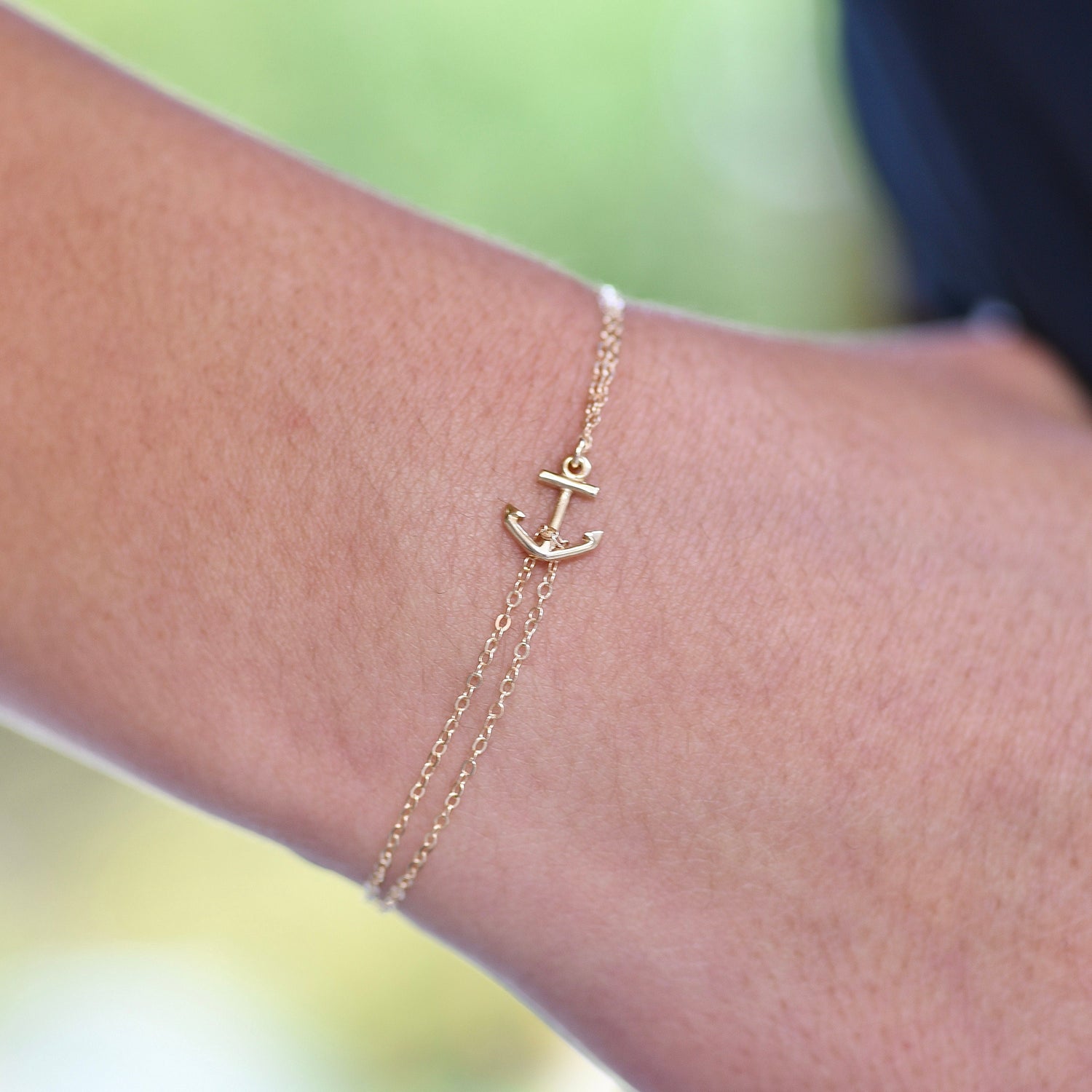 Gold anchor bracelet on a wrist with a blurred green background