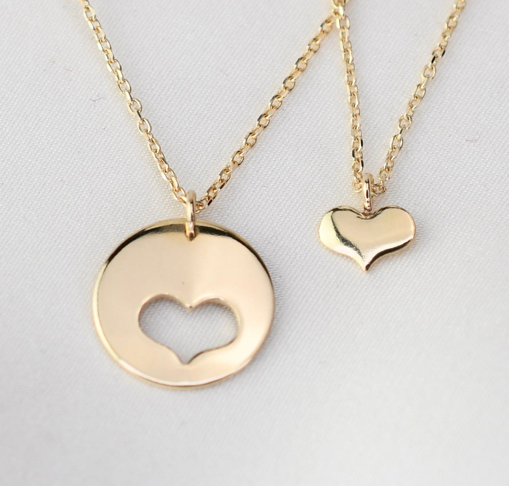 Two gold necklaces with heart-shaped pendants on a light gray background