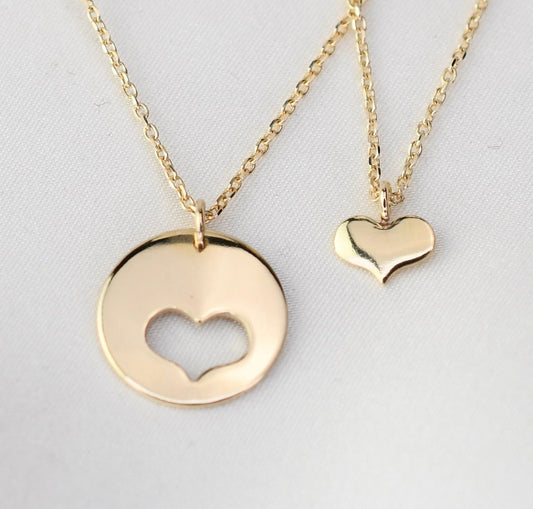 Two gold necklaces with heart-shaped pendants on a light gray background