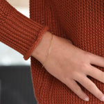 Gold bracelet on a wrist with a brown textured sweater