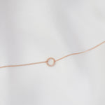 Rose gold bracelet with a small circular charm on a light gray background