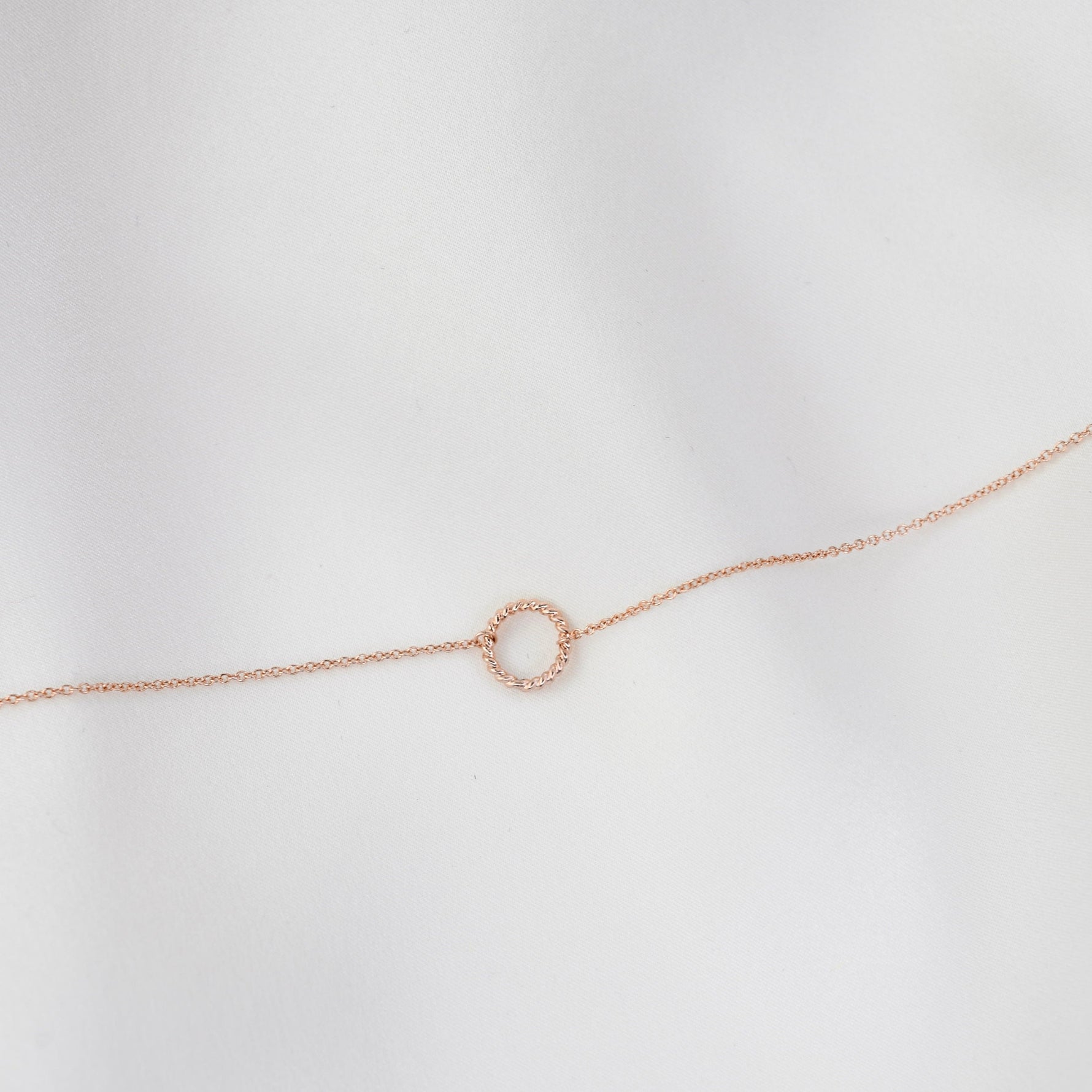 Rose gold bracelet with a small circular charm on a light gray background