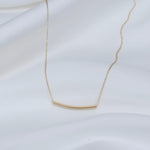 Gold necklace with a bar pendant on a white background