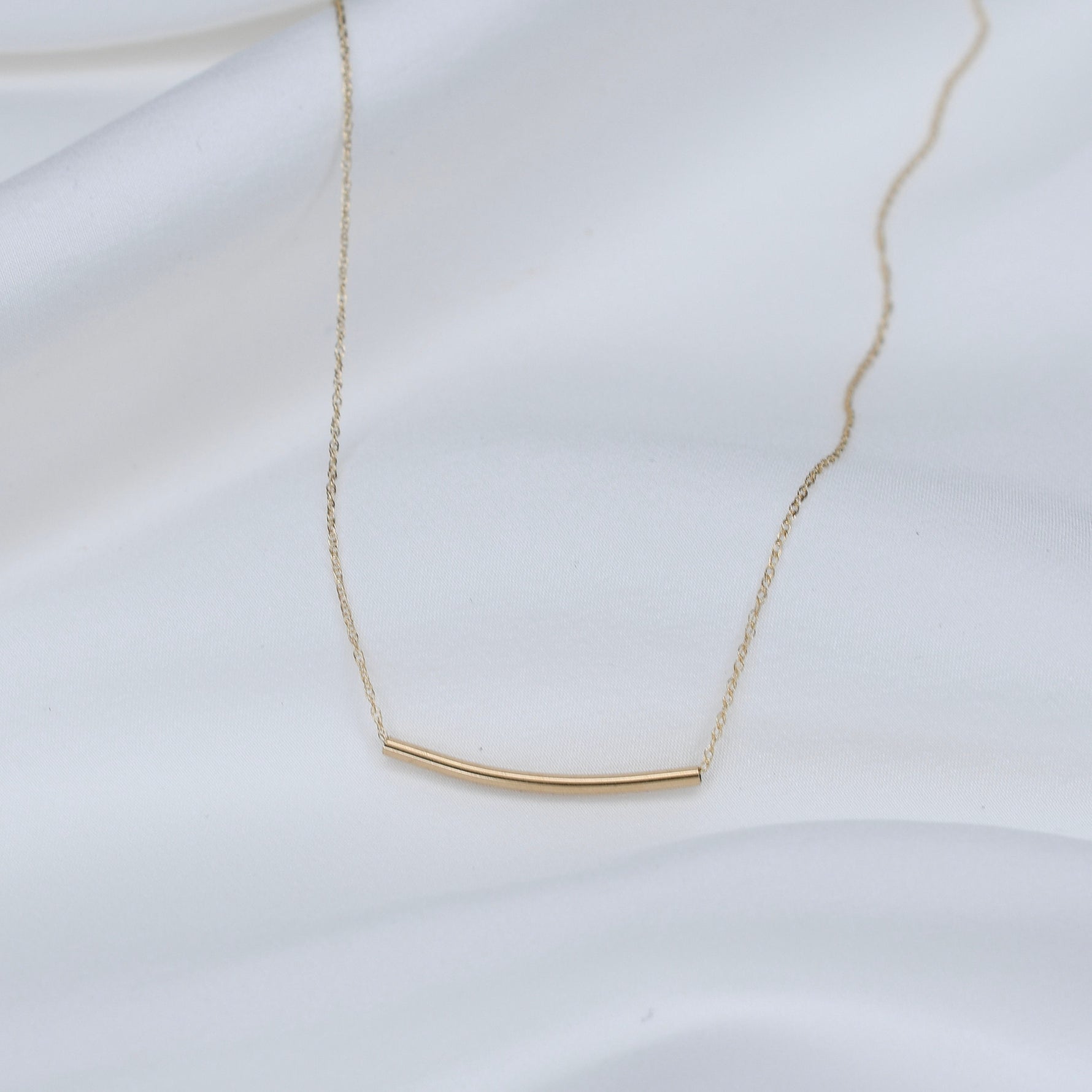 Gold necklace with a bar pendant on a white background