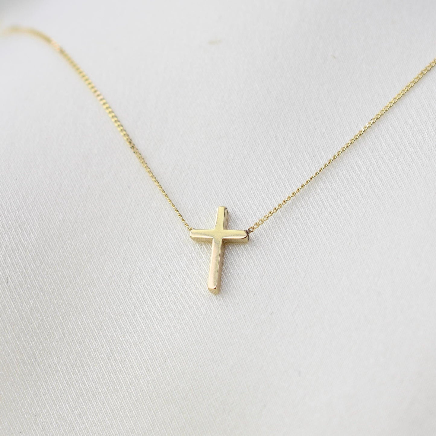 Gold cross necklace on a light gray background