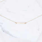 Gold necklace with a bar pendant on a white marble surface