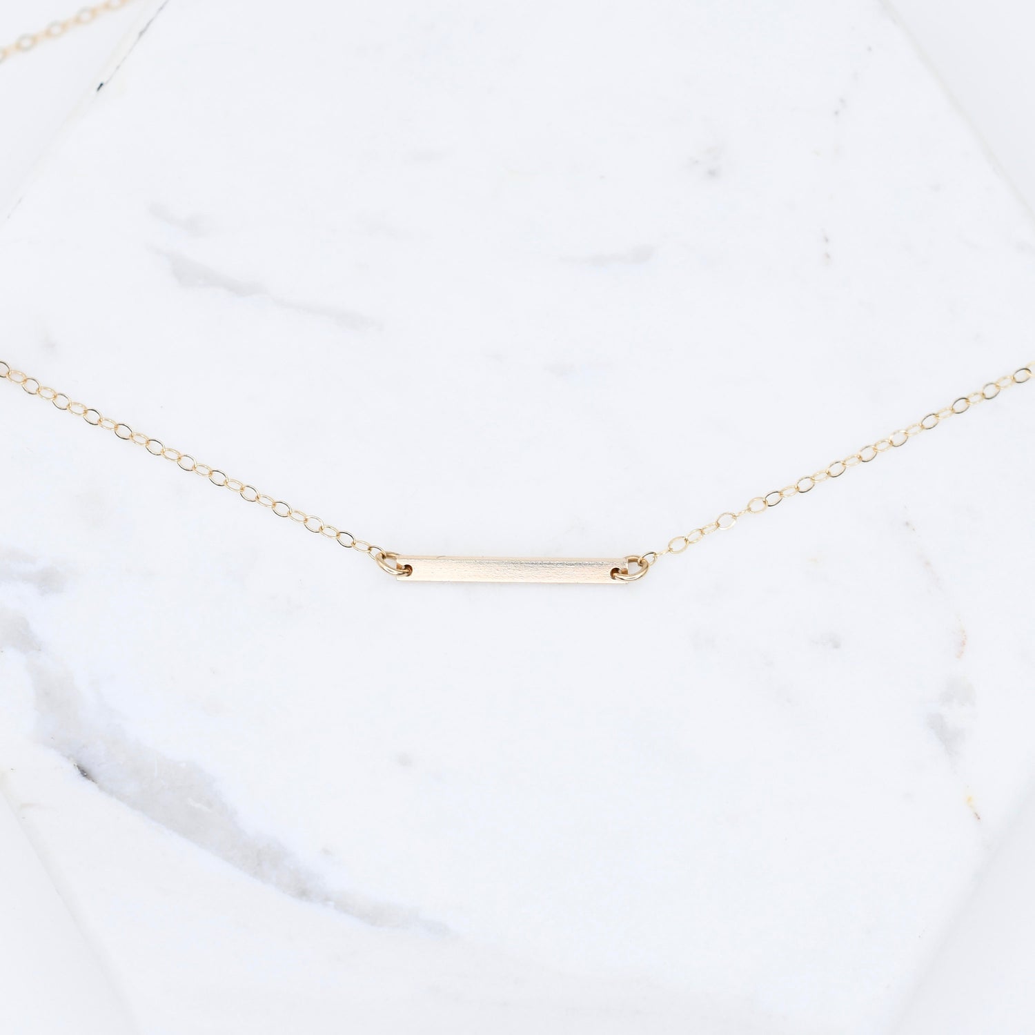 Gold necklace with a bar pendant on a white marble surface