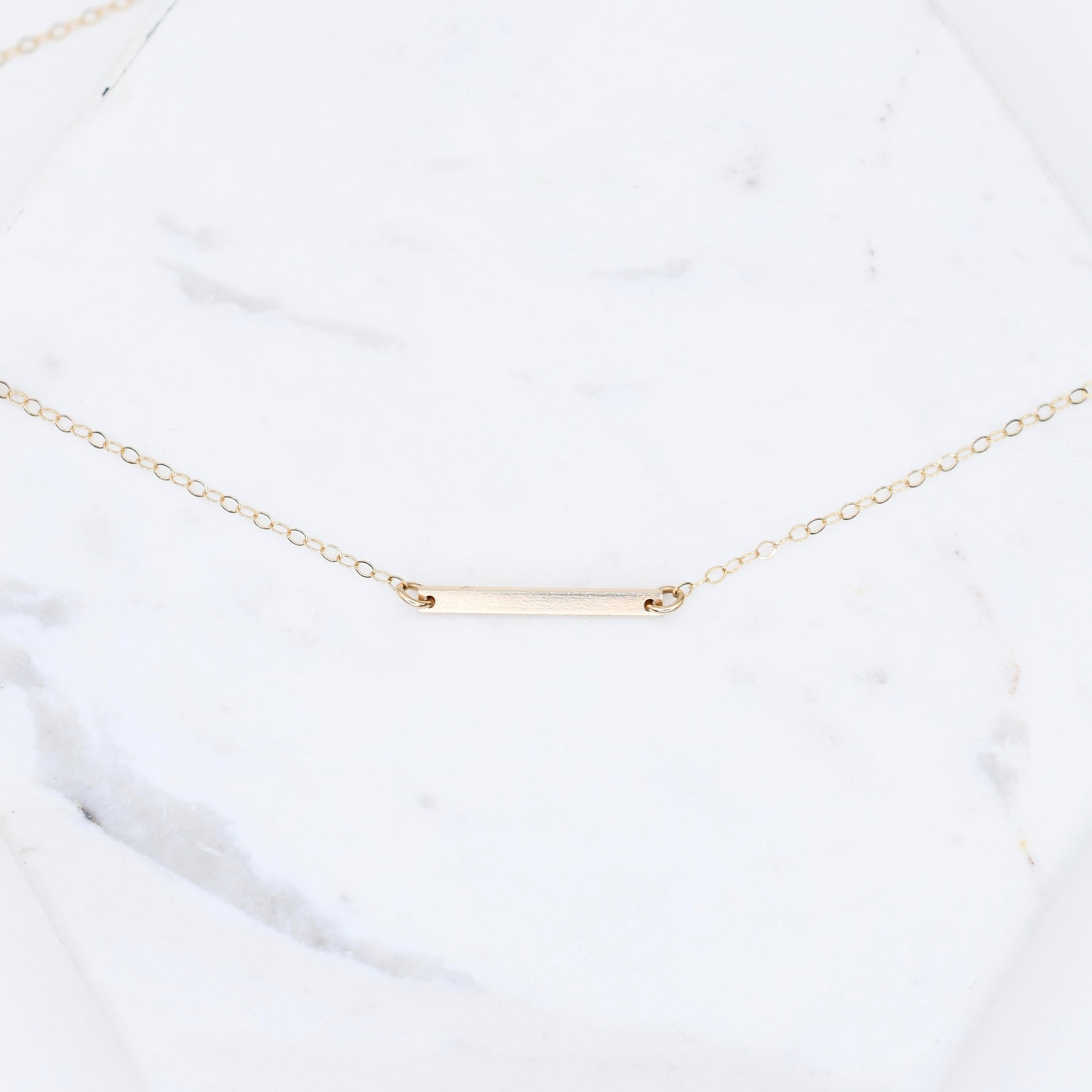 Gold necklace with a bar pendant on a white marble surface