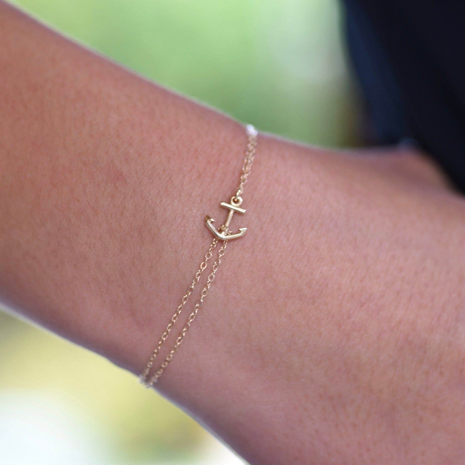 Gold anklet with an anchor charm on a person's ankle against a blurred background