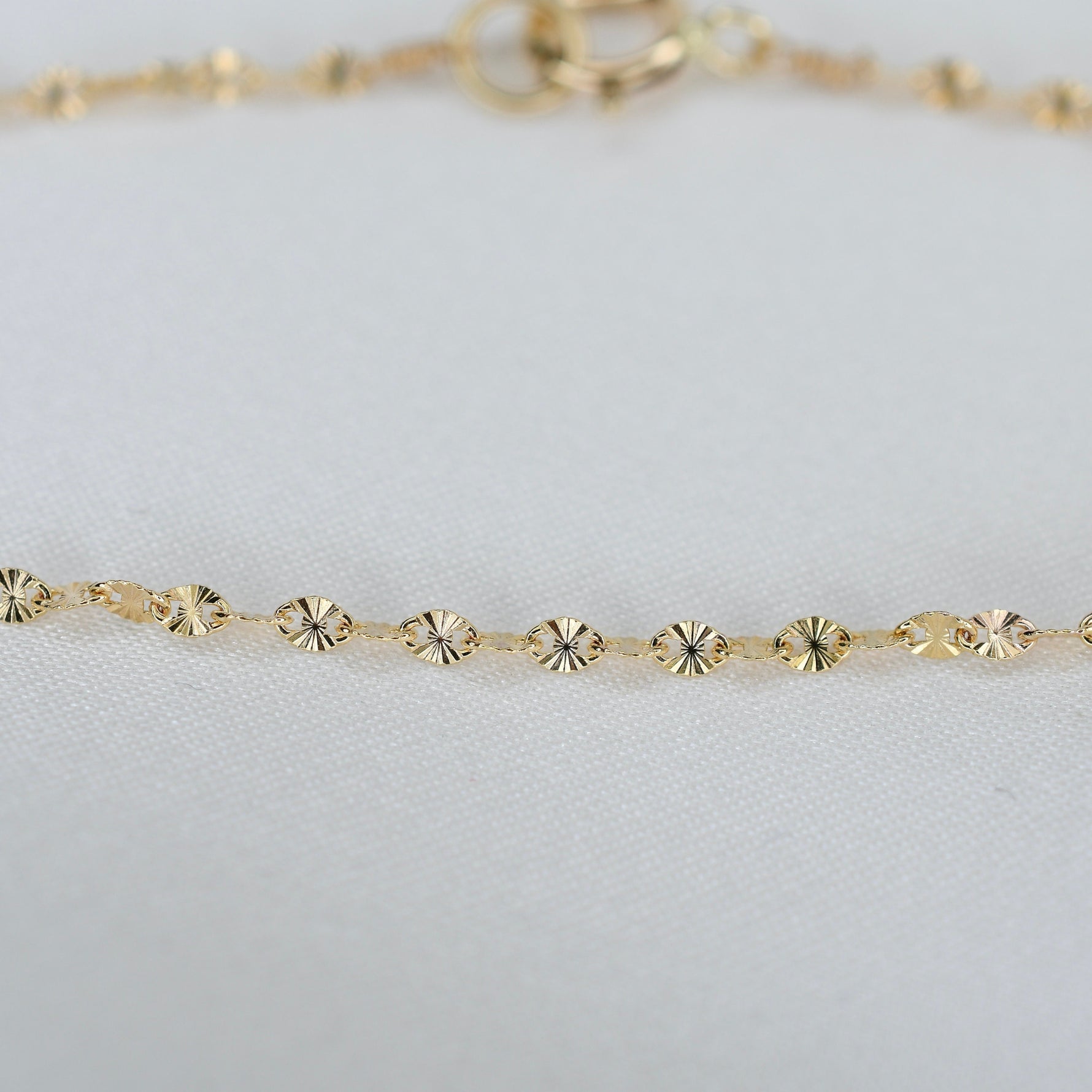 Gold bracelet with small circular links on a light gray background