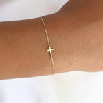 Delicate 14K gold side cross bracelet worn on wrist