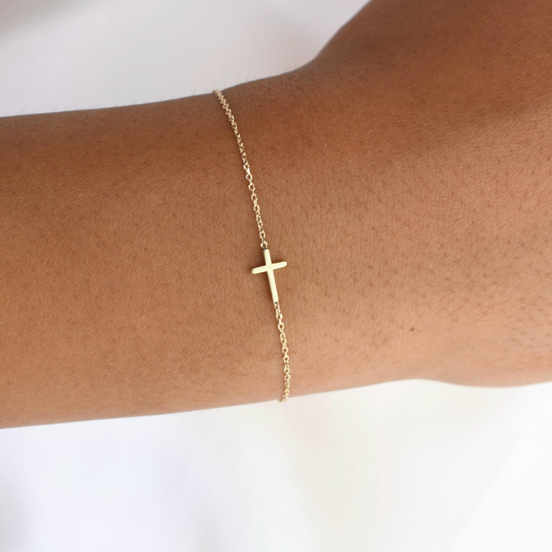 Delicate 14K gold side cross bracelet worn on wrist