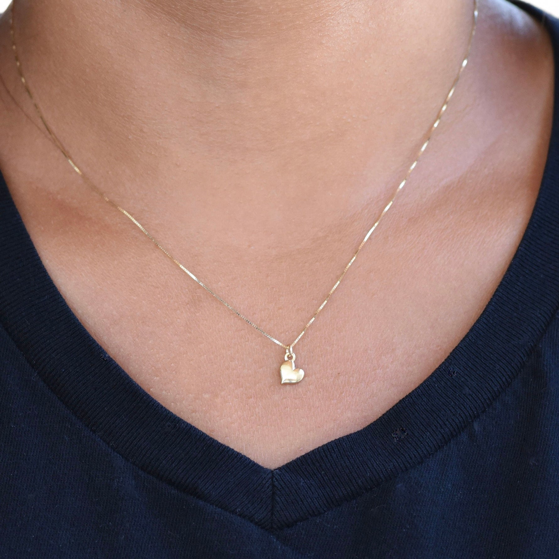 Gold heart-shaped pendant necklace on a person wearing a navy blue top.