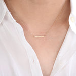Gold necklace with a bar pendant on a person wearing a white shirt.
