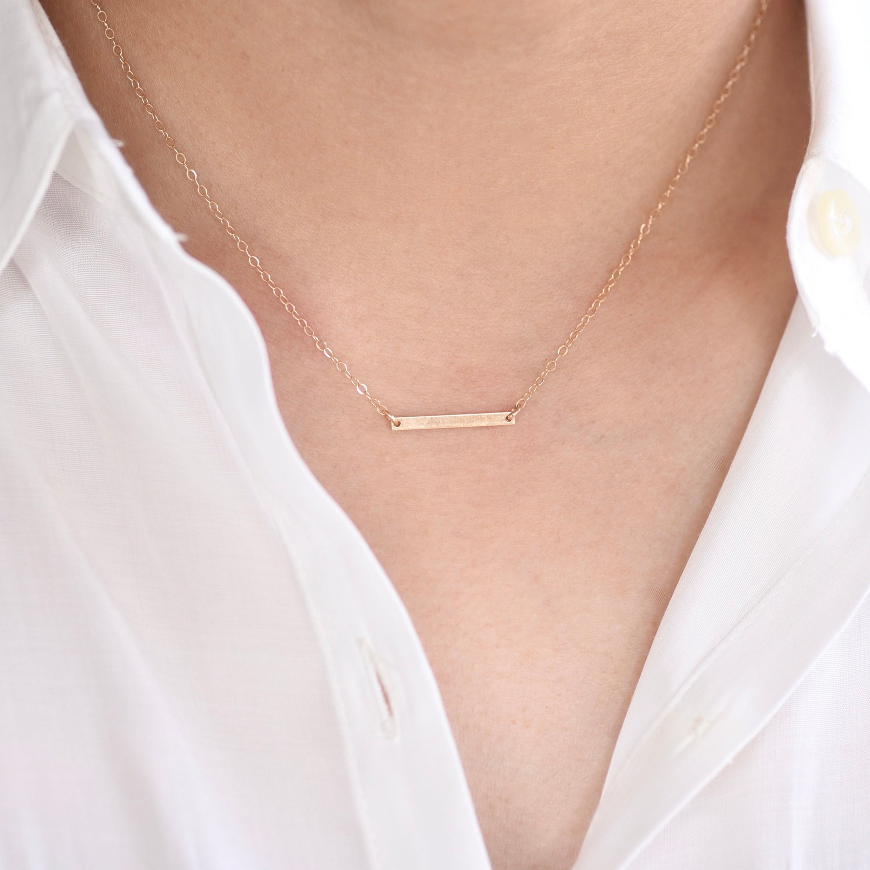 Gold necklace with a bar pendant on a person wearing a white shirt.