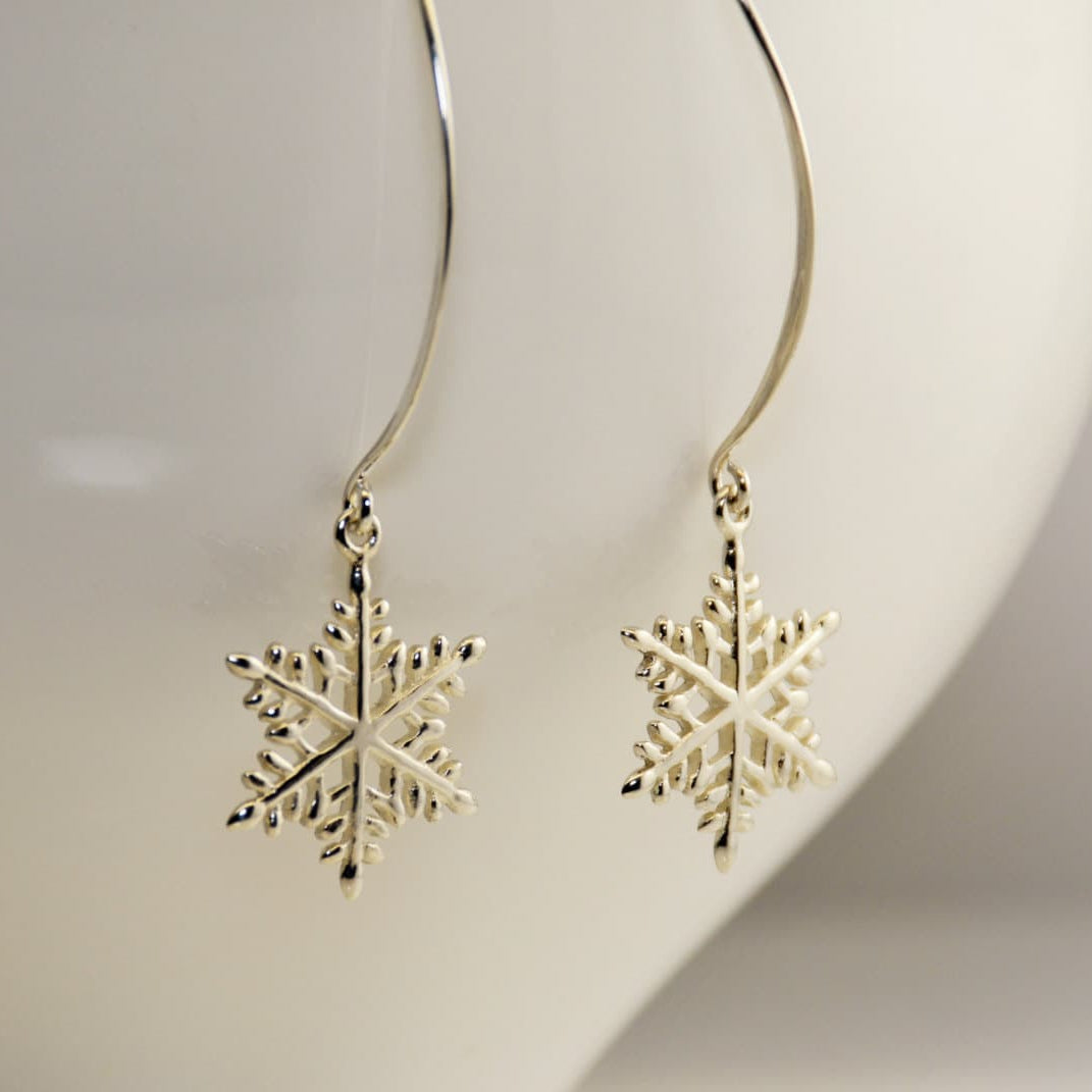 Gold snowflake earrings on a white stand
