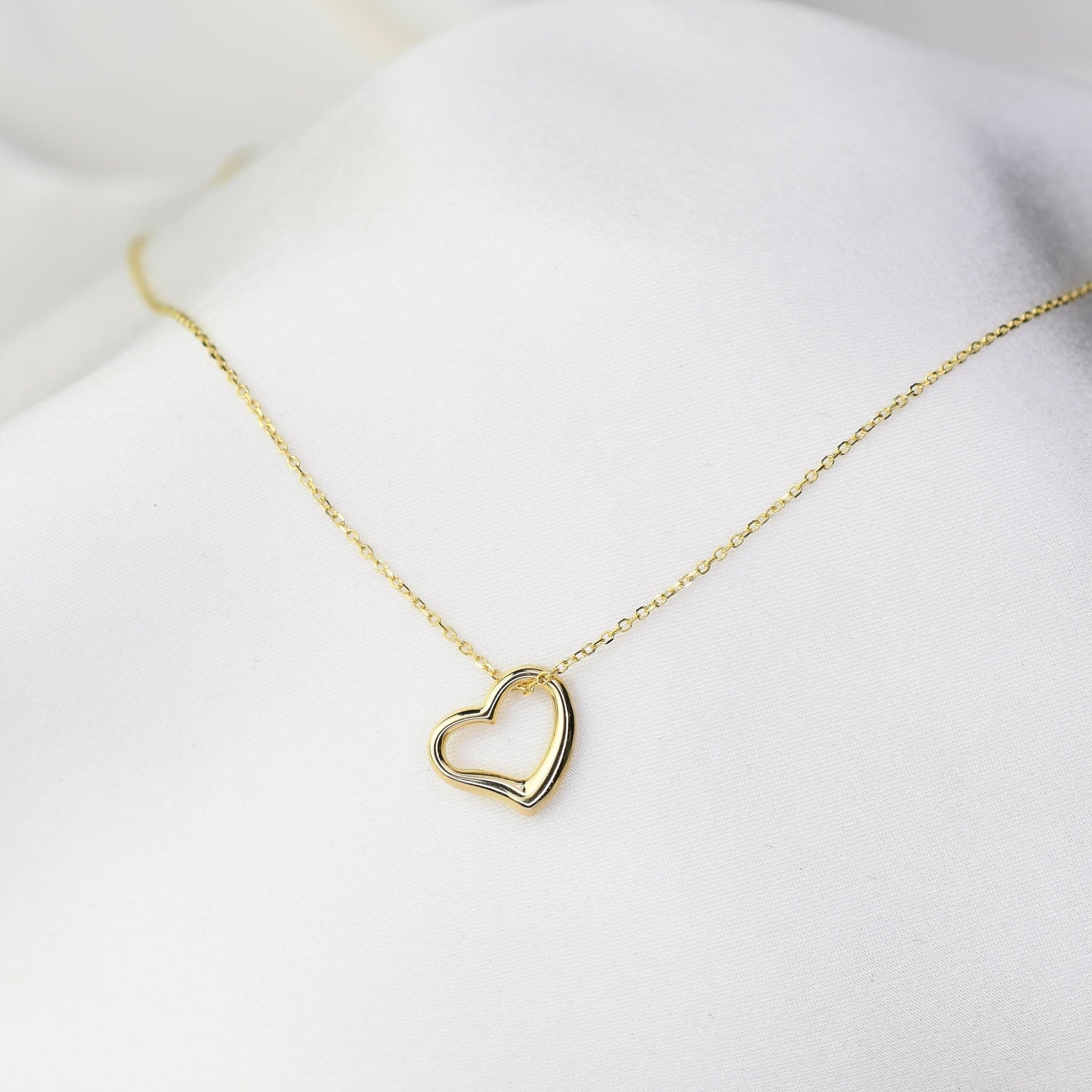 Delicate solid gold heart pendant necklace worn layered