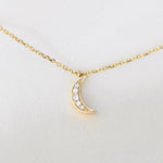 Gold crescent moon necklace with diamonds on a white background