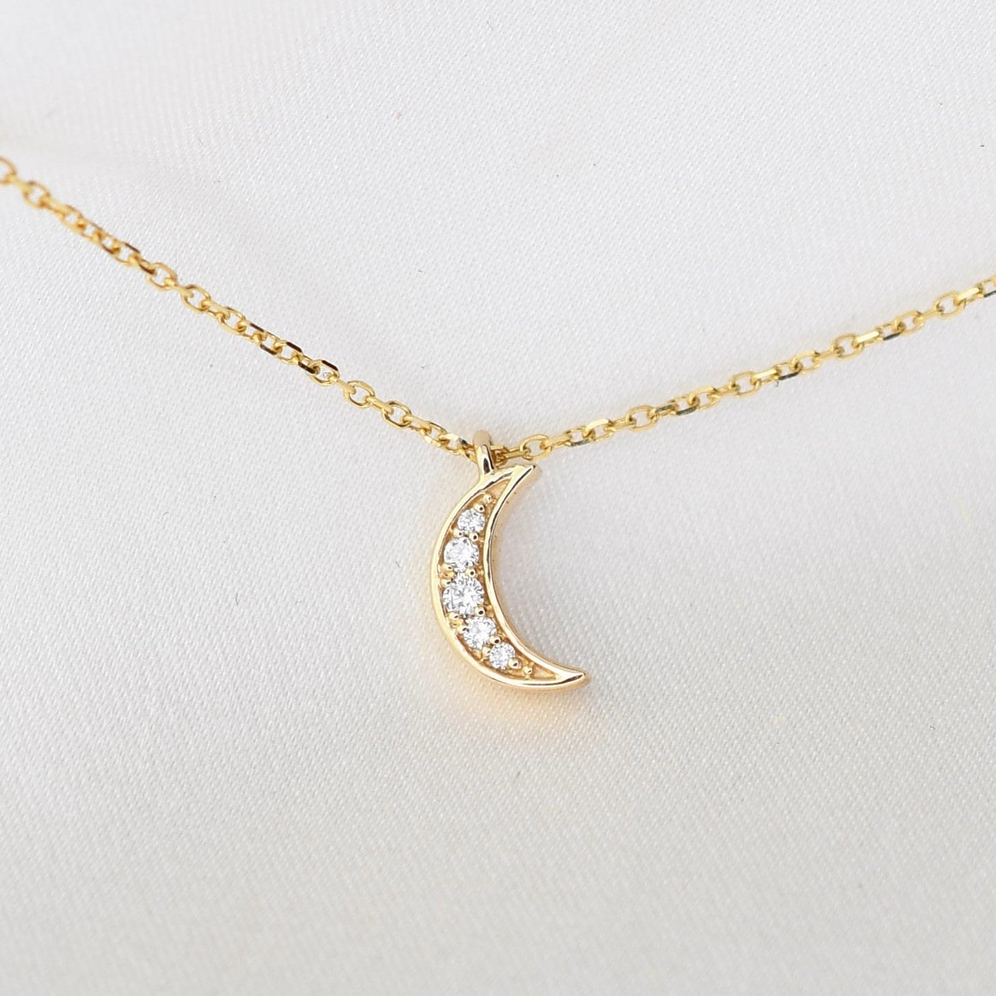 Gold crescent moon necklace with diamonds on a white background