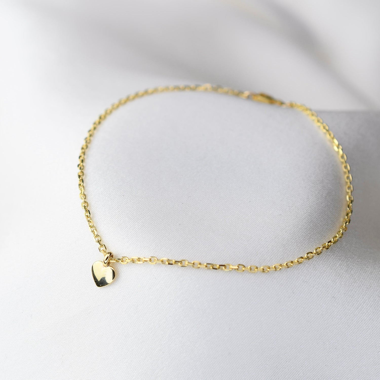 Gold bracelet with a heart charm on a light gray background